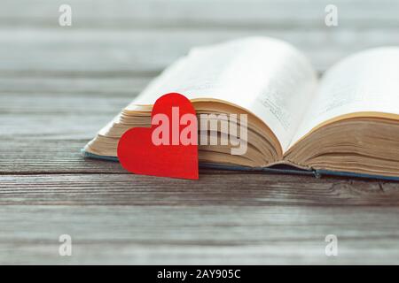 Open old book and red paper heart on wooden table, poetry and love lyrics concept