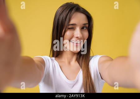 Pleasant attractive girl making selfie in studio and laughing. Good-looking young woman with brown hair taking picture of hersel Stock Photo