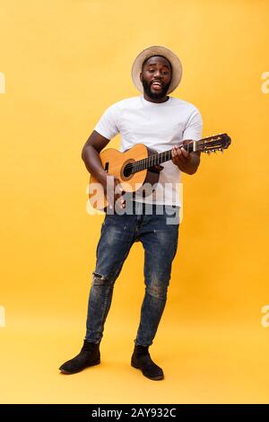 Full-length photo of excited artistic man playing his guitar in casual suite. Isolated on yellow background. Stock Photo