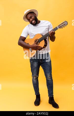 Full-length photo of excited artistic man playing his guitar in casual suite. Isolated on yellow background. Stock Photo