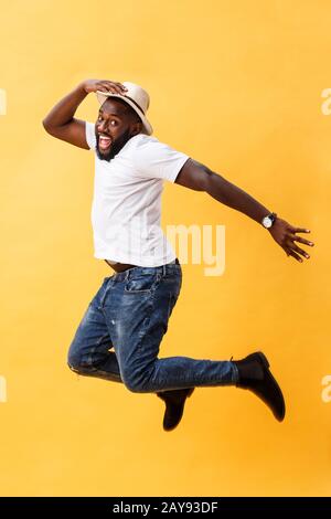 Full length of handsome young black man jumping against yellow background. Stock Photo