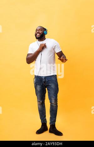 Full length portrait of a cherry young african american man listening to music with headphones and dancing isolated over yellow Stock Photo