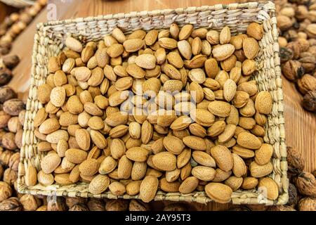 Close up of a basket of fresh, peeled almonds on sale at the local food market. Other dried fruits in the blurred background. Healthy snacks. Stock Photo