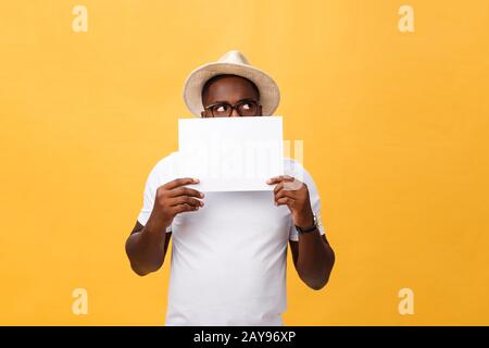 Young happy African-american hiding behind a blank paper, isolated on yellow background Stock Photo