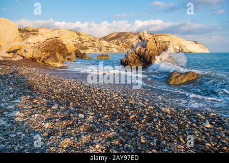 Afternoon view of breaking waves at the pebbly beach around Petra tou Romiou, also known as Aphrodite's birthplace, in Paphos, C Stock Photo