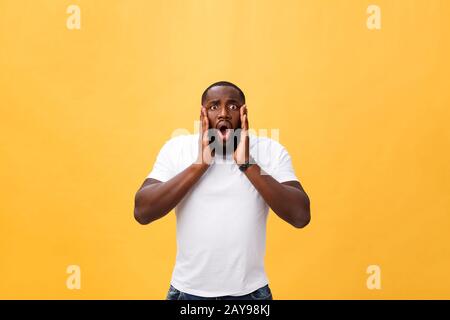 Amazed young African American hipster wearing white t-shirt holding hands in surprised gesture, keeping mouth wide open, looking Stock Photo