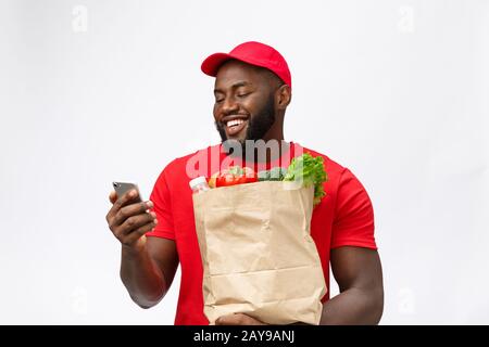 Delivery Concept - Portrait of Handsome African American delivery man or courier with grocery package and talking on mobile phon Stock Photo
