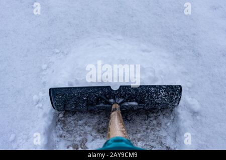 A snow shovel is seen pushing snow along a driveway from the perspective of someone shoveling their lane after a winter snowfall. Stock Photo