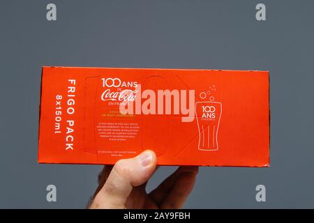 Paris, France - Jul 20, 2019: Man hand holding against gray background pack of Coca-Cola sweet drink 8 pack - French edition with 100 years of presence in France Stock Photo
