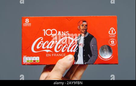 Paris, France - Jul 20, 2019: Man hand holding against gray background pack of Coca-Cola sweet drink 8 pack - French edition with 100 years of presence in France and black ethnicity man on cover Stock Photo