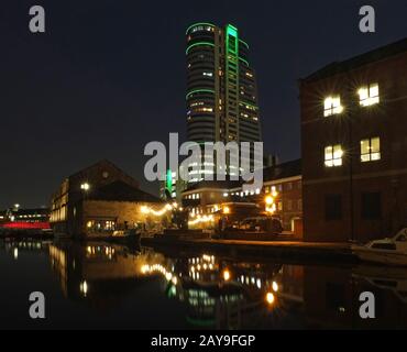 Cityscape view of canal wharfe in leeds at night with illuminated buildings and bridge reflected in Stock Photo