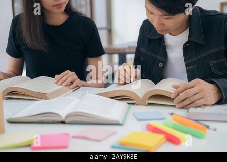 Learning, education and school concept. Young woman and man studying for a test or an exam. Tutor books with friends. Young students campus helps frie Stock Photo