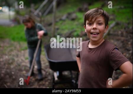Smiling boy in a brown t-shirt standing near wheelbarrow in yard Stock Photo