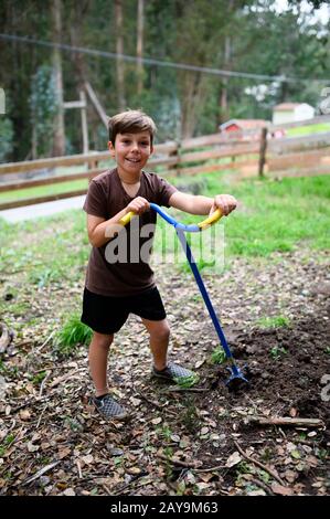 Boy smiling in the yard while he tills soil for a garden Stock Photo