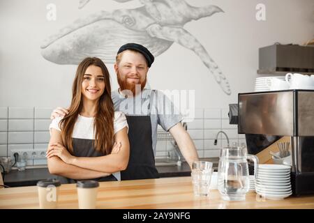 Coffee Business Concept - Positive young bearded man and beautiful attractive lady barista couple enjoy working together at the Stock Photo