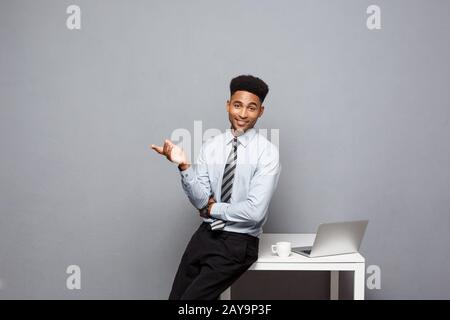 Business Concept - portrait of african american businessman talking and having coffee sitting at a desk using a laptop. Stock Photo