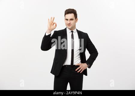 Business Concept: A handsome man in smart suit isolated on gray background showing ok sign. Stock Photo