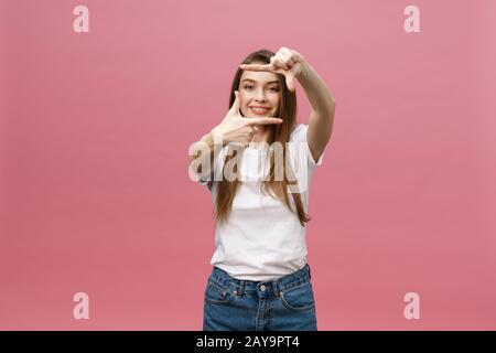 Cheerful young woman keeping mouth wide open, looking surprised, making hands photo frame gesture isolated on bright pink backgr Stock Photo