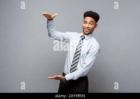 Business Concept - Amazed African American holding both hands on side presenting projects over grey background. Stock Photo
