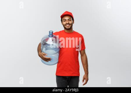 Delivery Concept - Handsome African American delivery man holding water tank. Isolated on Grey studio Background. Copy Space. Stock Photo