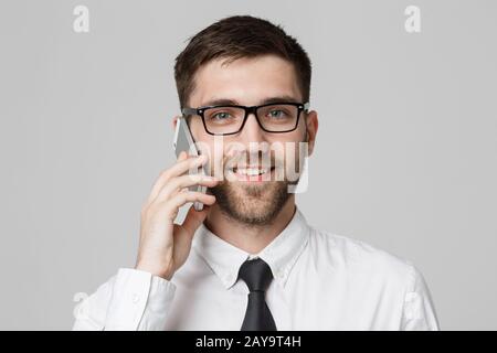 Business Concept - Portrait young handsome cheerful business man in suit talking on phone looking at camera. White background. C Stock Photo