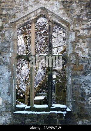 view through a window of a medieval ruined church in heptonstall yorkshire with snow covered trees Stock Photo