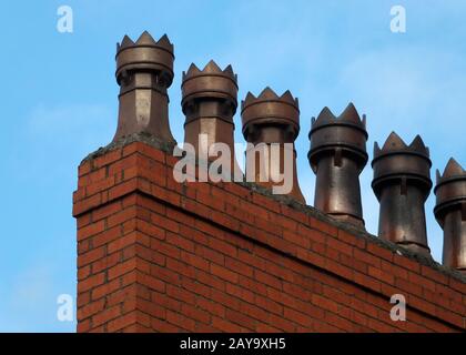 A row of old fashioned traditional clay chimney pots on a red brick support against a blue sky Stock Photo