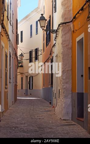 an empty picturesque narrow alley of old painted houses and street lamps in ciutadella menorca Stock Photo