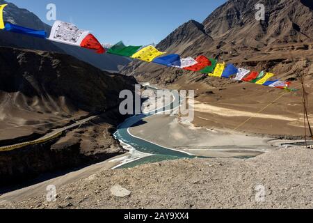 Prayer flags blowing in the wind above the confluence of the Indus and Zanskar rivers, Ladakh, India Stock Photo