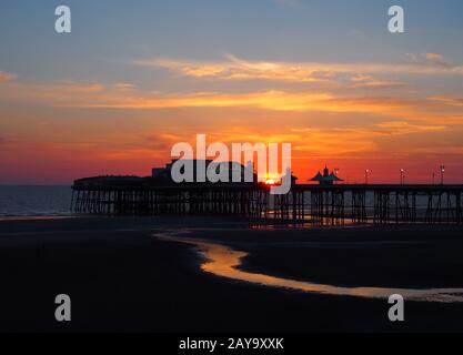 scenic view of blackpool north pier in glowing red evening light at sunset with illuminated pink sky Stock Photo