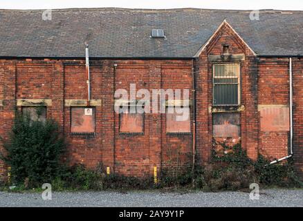 An old abandoned brick factory building with boarded up windows and crumbling decaying walls overgro Stock Photo