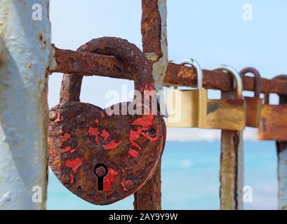 close up of an old heart shaped red rusty padlock chained to a railing with others in a line Stock Photo