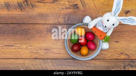 Seven colorful Easter eggs in a bowl held by Easter bunny with wooden background Stock Photo