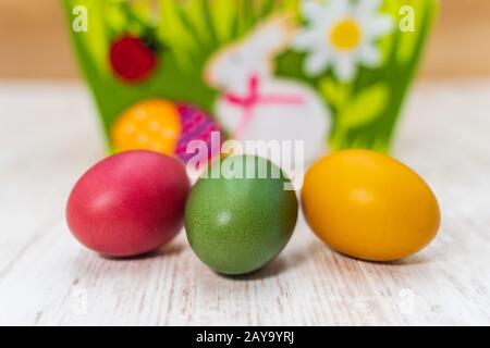 Three colorful Easter eggs in front of felt Easter basket with wooden background Stock Photo