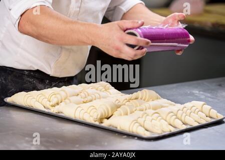 Pastry chef sealing with plastic film a tray of croissants dough. Stock Photo