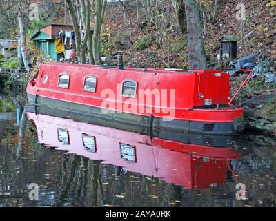 red narrow boat reflected in still water on the rochdale canal  surrounded by autumn  trees and shed Stock Photo