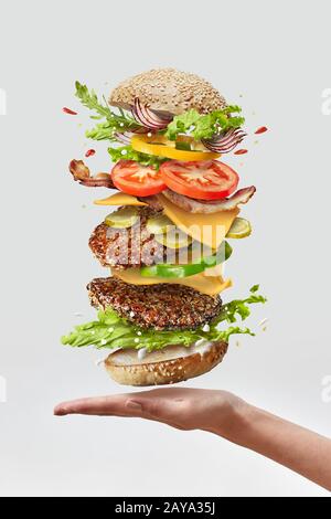 Deliciouse homemade burger on a woman hand with flying fresh ingredients on a white background. Copy space. Stock Photo