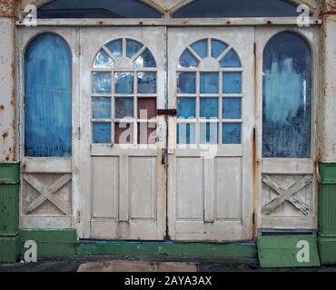 white wooden doors in an abandoned derelict house with broken and vandalized painted over windows Stock Photo