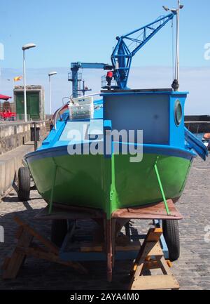 small green and blue old traditionial fishing boat on the dockside with crane in tenerife Stock Photo
