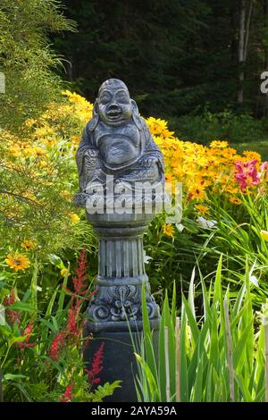Cement statue of Buddha on top of a column in border with red Astilbe 'Radius' and yellow Rudbeckia - Coneflowers in backyard Country garden in summer Stock Photo