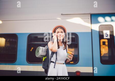 theme tourism and travel young student. beautiful young Caucasian girl in dress and hat standing at train station near train wit Stock Photo