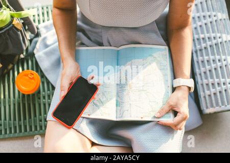 Theme travel planning. The top view hands Caucasian woman uses smart phone and studies the tourist map, passes route, navigates