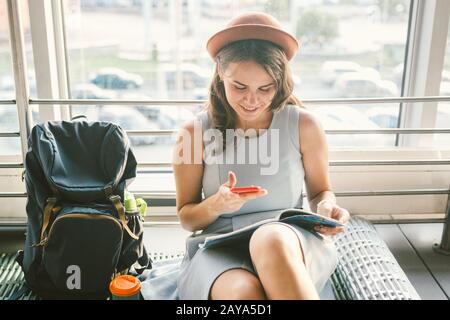 theme of tourism and travel of young student. Beautiful young caucasian girl in dress and hat sits on floor tourist rug inside t Stock Photo