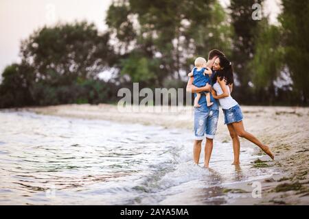 Young beautiful and stylishly dressed family of three people mom, dad and daughter of one year on the shoulders of a man walking