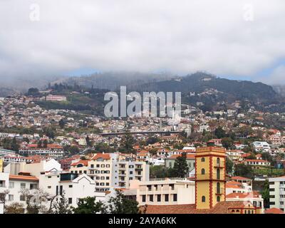 cityscape view of funchal in madeira with typical white painted buildings old church and bridge with tree covered mountains unde Stock Photo