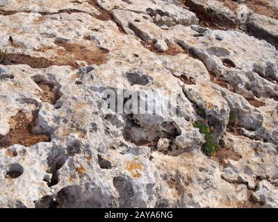 rough grey eroded limestone ground on a beach with scattered sand Stock Photo