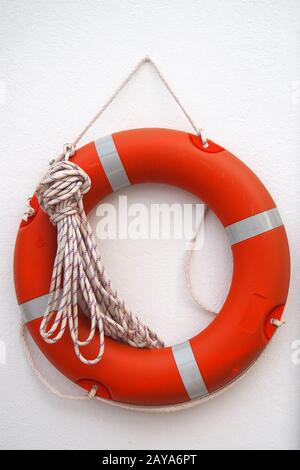 a round orange lifebelt with safety rope hanging on a white wall Stock Photo