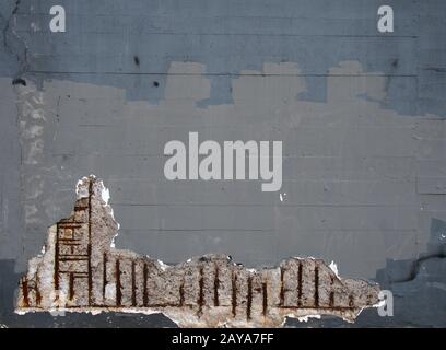 an old grey painted concrete wall with corroding rusty steel reinforcement bars causing damage to the structure Stock Photo