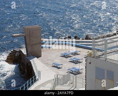 the public lido in funchal madeira with concrete diving platform sun loungers and steps to a sunlit blue sea Stock Photo