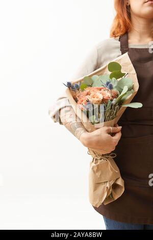 Woman with red hair holds beautiful colourful blossoming flower bouquet of fresh roses living coral color on a white background. Stock Photo